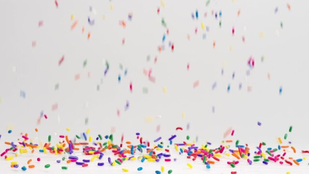 Birthday party celebration rainbow sprinkles raining down and bouncing off white table top in slow motion