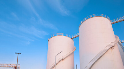 Low angle view of storage fuel tanks with oil pipeline system in petroleum industrial area at harbor against blue sky background
