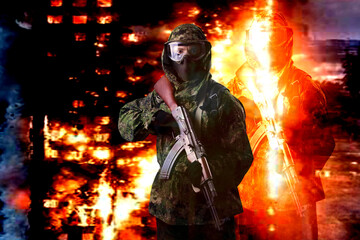 A soldier in camouflage uniform with a rifle against the backdrop of a burning destroyed house, looks into the camera. The concept of war or the game of airsoft