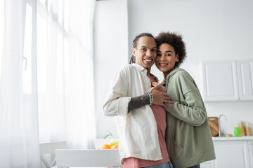 Fototapeta premium Smiling african american couple looking at camera and hugging at home.