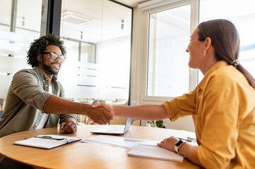 Handsome positive businessman looking at the female colleague, they shaking hands. Collaboration of business partners, workteam, support and agreement concept