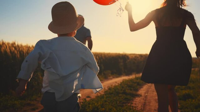 Active happy family run together on wheat field. Enjoy summer walk in nature. Mom hold balloons in hands, dad and boy spread arms to sides and feeling freedom. Tourism, travel, hike. Leisure activity.