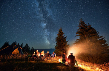 Night camping in mountains under starry sky. Group of people hikers having a rest near campsite,...