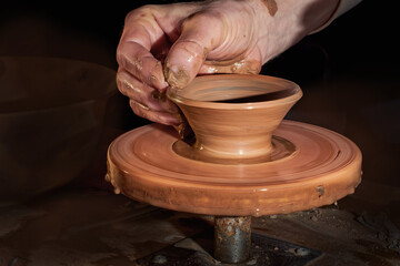 Potter's hands in the process of working on the wheel. Making a clay bowl close-up. Creative process with dark background