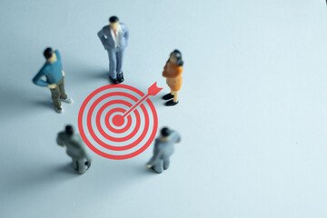 A Business group  standing in a circle, with all eyes focused on bullseye target icon over white...
