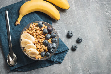 Granola cereal oatmeal with blueberries and banana fruits in a bowl on a grey background, top view