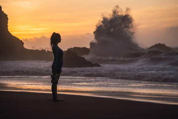 woman walking on the beach with her shoes in her hand while looking at the sea. sunset on the island of tenerife Spain