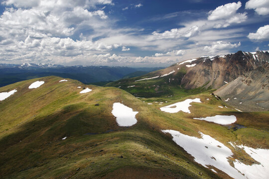 Mountain landscape of green spring valley with rocks and snow on the background of high range under blue sky Altai Siberia Russia