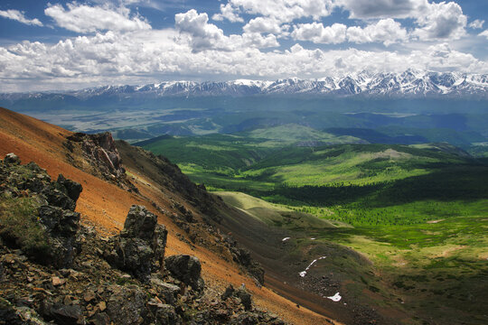 Dramatic sunset mountain landscape of green spring hills with rocks and snow on the background of high range under blue sky Altai Siberia Russia