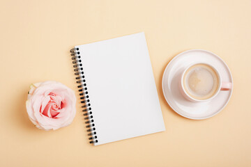 Coffee in cup, rose flower and spiral notebook on neutral background. Top view, flat lay, mockup