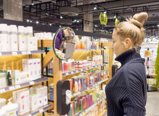 Woman buying make up at cosmetics section in store. choosing cosmetics, perfumes, creams and shampoos, Using tester.