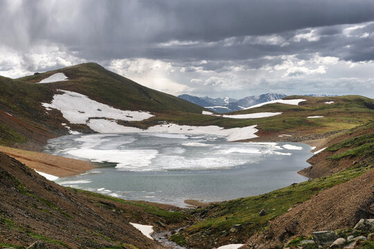 Frozen highland lake among dramatic mountain green hills with snow at gloom weather Altai Siberia Russia