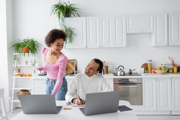 African american couple using laptops in kitchen in morning.