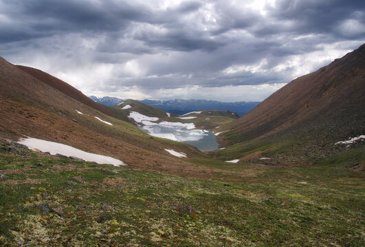 Frozen highland lake among dramatic mountain green hills with snow at gloom weather Altai Siberia Russia