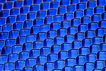 A pattern of metal grid cells in a blue glow. Close-up macro shot.