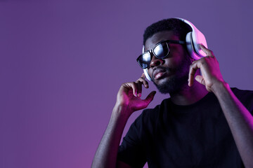 Young African American man in sunglasses and headphones listens to music and dances.