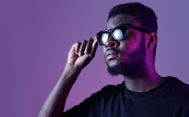 Stylish african american man in sunglasses and on dark neon background.