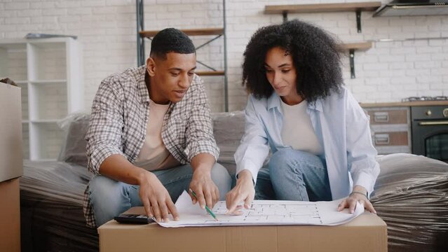 African American young couple discussing blueprint of renovating house while moving into new house