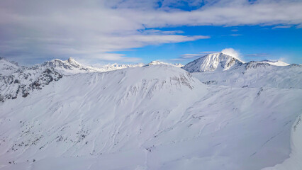 Panoramic view of austrian alps in Winter. High peaks covered with snow and clouds on a sunny winter day.