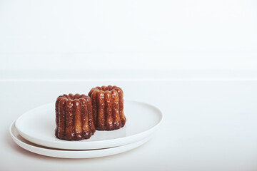 Delicious freshly baked canele, rum and vanilla flavored french pastry with caramelized crust on white plate against white background. Copy space.. A specialty of the Bordeaux region of France.
