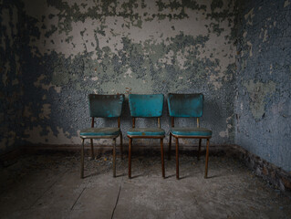 A row of blue chairs and a wall of chipping paint in an abandoned hospital