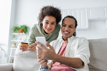 Obraz na płótnie Canvas Smiling african american couple using smartphone during online shopping at home.
