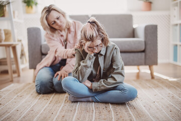 Mother taking pity on her daughter sitting on the floor. - 571220941