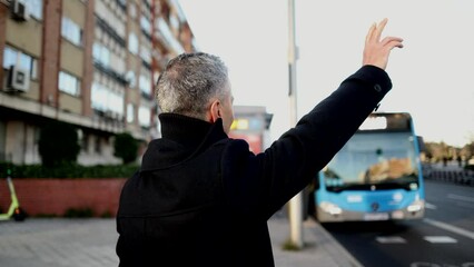 Smiling mature businessman standing on the city street, raising his hand to hail a taxi, public transport, bus,
