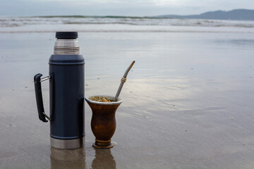 termo de acero y porongo con yerba mate sobre la arena frente al mar, bebiendo un mate argentino...