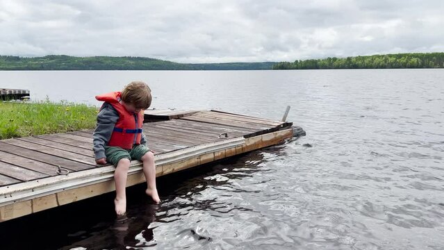Young boy at the cottage dipping feet in water