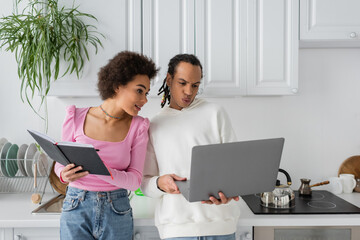 African american couple working with laptop and notebook in kitchen.