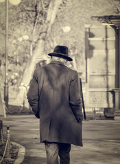 Rear view of a lonely old man with a hat walking in the park. Vintage black and white photography.