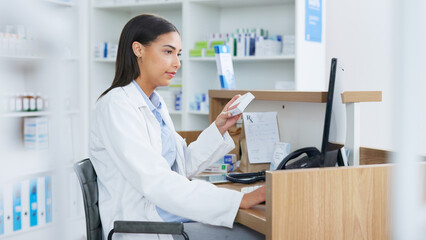 Young pharmacist working on computer at a pharmacy counter. Woman using technology to access drug...