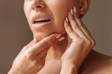Cropped shot of young woman suffering from jaw pain holding her chin with hands on brown...