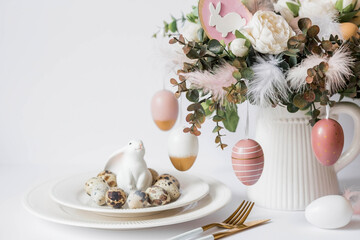 Banner. The concept of a bright Easter holiday. A bouquet of flowers with feathers, white rabbits and Easter eggs in a plate on a white isolated background. Beautiful Easter card.
