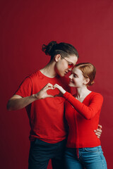 Valentine Couple Portrait of Smiling and Hugging Beauty Young Woman and her Handsome Boyfriend man making shape of Heart sign Hands. Valentines Day.