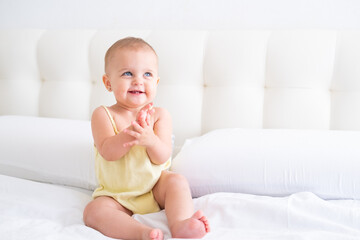 Obraz na płótnie Canvas portrait of cute smiling baby girl in yellow bodysuit on white bedding. Healthy newborn child