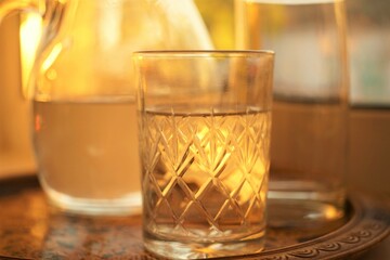 Glass of water and jug of water in a tray on the sunny windowsill.