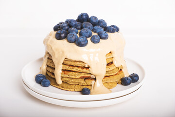 Delicious freshly cooked thick and fluffy gluten free pancakes stacked on white plate, served with cashew cream and fresh blueberries. Healthy food