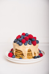 Delicious freshly cooked thick and fluffy vegan protein pancakes stacked on white plate, served with cashew cream and fresh berries. Healthy food. Copy space.