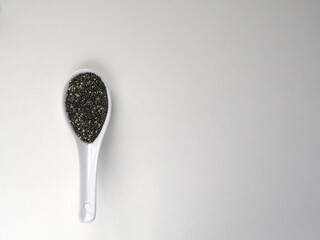 White ceramic spoon with Chia seeds on white wooden table.