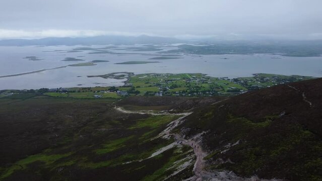 Aerial tracking shot of people walking down mountain trail in Ireland