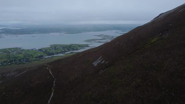 Aerial reveal of hiking trail on Irish mountain, with stunning ocean vista in background