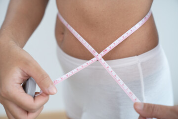 Concept of weight loss. Girl holds jeans in her hand and shows a thin waist and measures her waist...