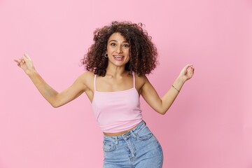 Woman with curly afro hair model poses on a pink background in a pink T-shirt, free movement and dance, look into the camera, smile with teeth and happiness, copy space