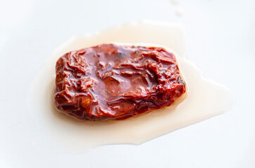 Close-up of one piece dried or sun-dried red tomatoes with oil on white ceramic plate