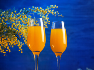 Mimosa cocktail with flowers on a blue background. Copy space