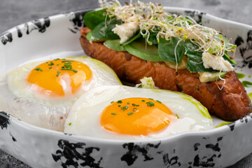 Two fried eggs for breakfast with avocado toast and salad on a plate. Healthy breakfast on the table, close up