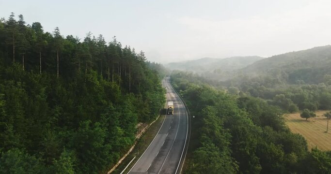 Highway traffic from behind  congested highway mountains on hot summer day top view of tree crowns forest at sunset. Aerial view flow of cars along highway. Environmental pollution