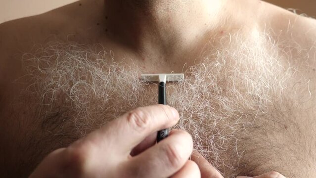 A man shaves the long gray hair on his chest.
